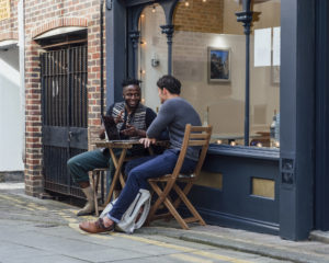 Two men sitting outside a coffee shop discussing social equity.